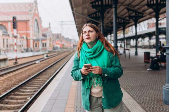 Young worried woman traveler with small backpack on the railway station, 30s redhead women waiting for train. Tourism, solo vacation