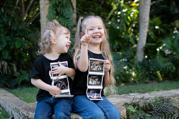 Pregnancy announcement by siblings. Social media pregnancy announcement. Big sister. The third child in a family. Two kids holding a sonogram of a new baby  - obrazy, fototapety, plakaty