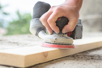 Close-up on a wooden board being sanded with an eccentric sander.