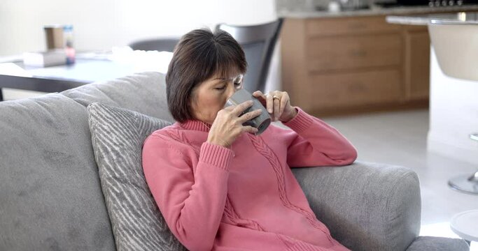 Stylish attractive mature woman relaxing drinking morning coffee enjoying sitting on sofa