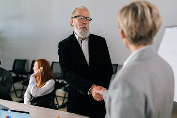 Fototapeta premium Back view handshaking unrecognizable middle aged female CEO and mature businessman partner after signing contract at group negotiations, successful business deal, closeup, rear view, selective focus.