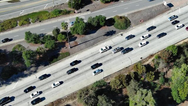 overhead aerial footage of cars and trucks driving on the 110 freeway near Dodgers Stadium surrounded by lush green trees, plants and grass in Los Angeles California USA