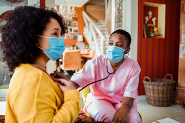 Female caregiver examining patient with stethoscope at home