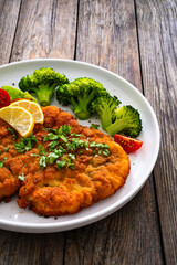 Crispy breaded fried chicken cutlet with boiled broccoli and fresh vegetables on wooden table
