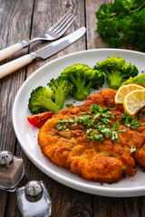 Crispy breaded fried chicken cutlet with boiled broccoli and fresh vegetables on wooden table

