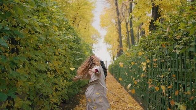Woman throws leaves up, spins around axis against background of amazing green garden with hedge