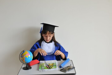 formanda infantil com beca e capelo uniforme de formatura em mesa escolar com globo terrestre 