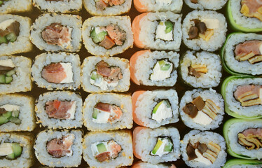 Close-up of a lot of sushi rolls with different fillings lie on a wooden surface. Macro shot of cooked classic Japanese food with a copy space.