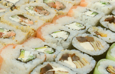 Close-up of a lot of sushi rolls with different fillings lie on a wooden surface. Macro shot of cooked classic Japanese food with a copy space.