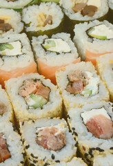 Close-up of a lot of sushi rolls with different fillings lie on a wooden surface. Macro shot of cooked classic Japanese food with a copy space.