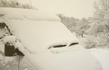 Fragment of the car under a layer of snow after a heavy snowfall. The body of the car is covered with white snow