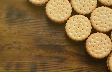 A round sandwich cookie with coconut filling lies in large quantities on a brown wooden surface. Photo of edible treats on a wooden background with copy space