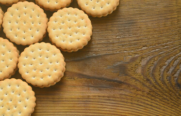 A round sandwich cookie with coconut filling lies in large quantities on a brown wooden surface. Photo of edible treats on a wooden background with copy space