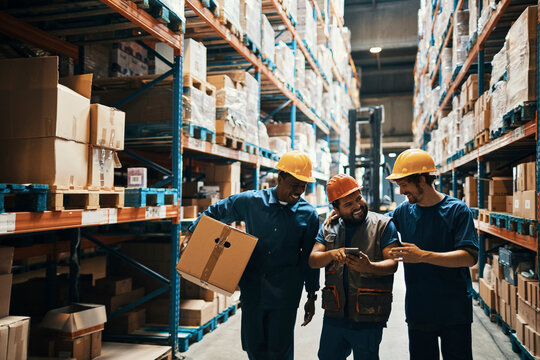 Diverse group of warehouse workers using a smartphone while carrying boxes and working in a warehouse