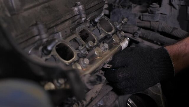Close-up of a mechanic in gloves disassembling the engine under the hood of a car at a service station. Engine repair in the workshop. A man makes a major repair of a car in a car service station.