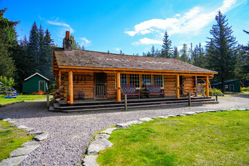 Log house of the Historic Taku Glacier Lodge, a wooden cabin located on the shores of a melt water lake in the mountains north of the Alaskan capital city Juneau - obrazy, fototapety, plakaty