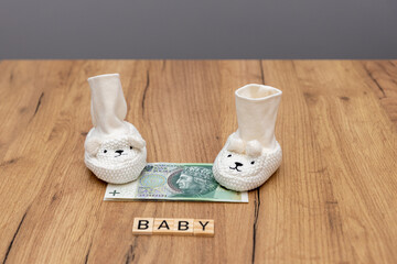 Tiny baby socks on the table with unfolded banknotes in denominations of zloty. 
The concept of the impending birth of a child and care for the state in the form of social 500 plus