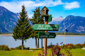 Directions signs to a forest trail and to the Taku General Store in the park of the Taku Glacier Lodge, on the shores of a melt water lake in the mountains north of the Alaskan capital city Juneau - Powered by Adobe