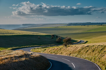 Winding curvy rural road leading through the countryside bathed in warn sunlight in Sussex, England.