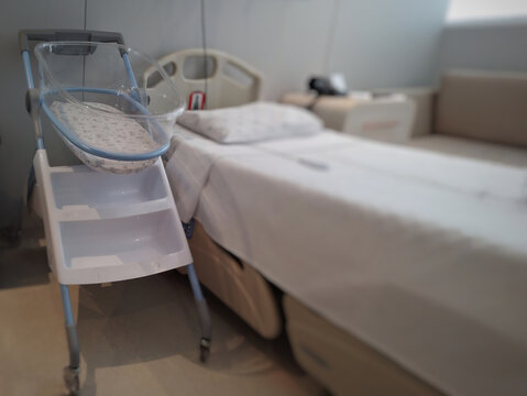 Acrylic crib for newborn, next to the bed in a maternity room.