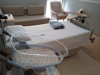 acrylic crib for a newborn in the foreground, in the background the bed and furniture in a maternity room