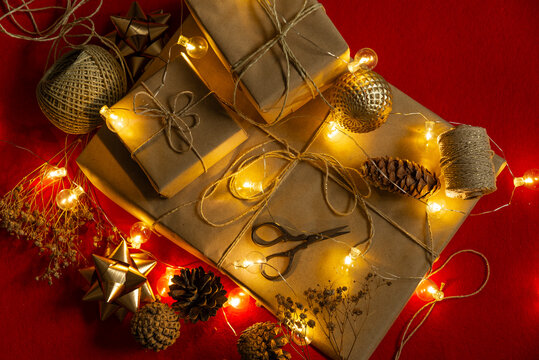 Paquetes De Regalo Envueltos Con Lazos Y Luces De Navidad, Piñas Y Tijeras Sobre Fondo Rojo.