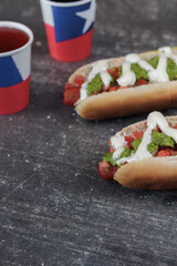 Completo Italiano Chileno: hot dog bun with vianesa, tomato, palta and mayo with poly paper cups chilean flag on chilean national holidays. on cement table. Vertical Typical Chilean food concept