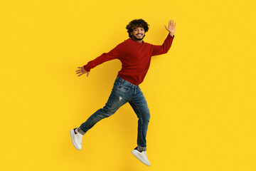 Fototapeta na wymiar Excited young indian guy jumping over yellow background