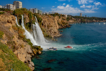 Fototapeta na wymiar The moment when the Lower Düden waterfall flows into the sea, against the background of the steep shores of the Mediterranean and the urban development of the city of Antalya.