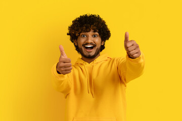 Excited millennial indian man showing thumb ups on yellow