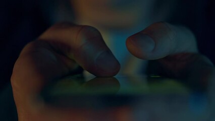 Close-up of a modern smartphone user's hands. Fingers scroll through the pages of social networks looking through bright pictures and photographs of other bloggers. Smartphone screen flickers at night