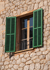 Window with open green, wooden shutters in a stone wall. Mallorca, Spain