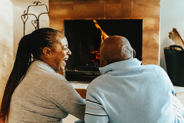 Senior African couple by cozy fireplace having fun together inside rural house. Elderly life style family and relationship concept
