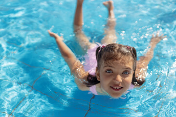 Portrait of happy 7 years old girl swimming in swimming pool on sunny day