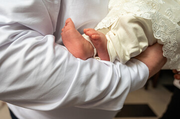 Fototapeta premium a man and a girl hold a small child in their arms before baptism. The legs of a small child