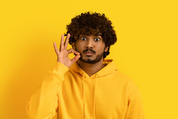 Handsome indian guy zipping his mouth on yellow background © Prostock-studio