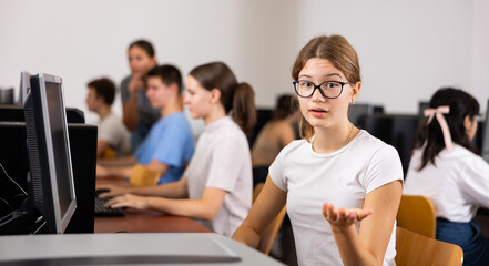Portrait of girl student looking at camera making hand gesture while using computer in classroom in college - obrazy, fototapety, plakaty