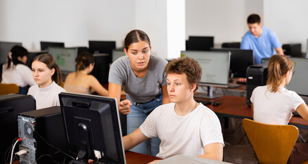 Fototapeta premium Woman teacher helps guy with learning on computer in school class