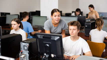 Young female teacher working with schoolboy in computer class of school library