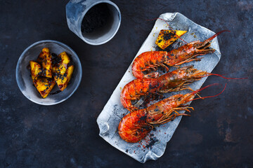Traditional fried king prawns with pineapple pieces and black salt served as top view on a design tray with text space