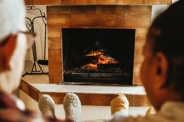 Multiracial senior friends by wood fireplace warming inside rural living room. Winter, spring and...