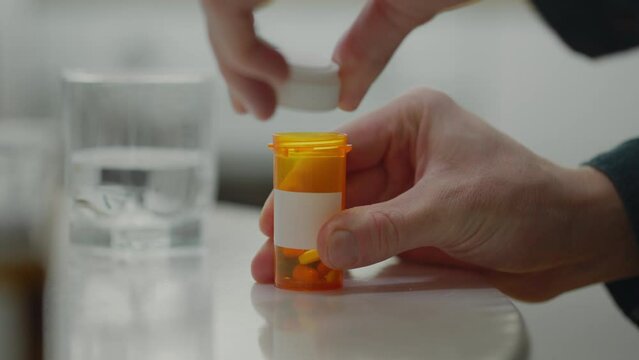 A Caucasian man diagnosed with depression follows a strict schedule of taking pills, pouring them from an orange bottle into his palm. Schedule prescribed by a psychologist, appointment every day
