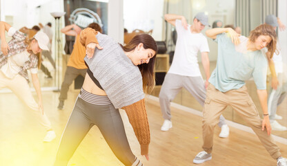 Portrait of cheerful hispanic teenage girl practicing hip-hop movements during group dance lesson...