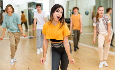 Portrait of expressive hispanic teenage girl practicing energetic dance movements with group of teens in choreography class .