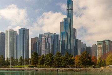 A beautiful autumn landscape along Lake Michigan with skyscrapers, hotels and office buildings in the city skyline, green water and autumn trees, blue sky and clouds in Chicago Illinois USA