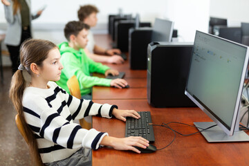 Focused teenage girl studying with classmates in modern computer lab at college ..