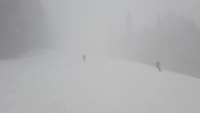 Blizzard of snow and wind on a ski slope. Skiers skiing in extreme conditions with fog and low visibility.