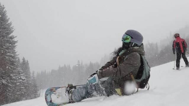 snowboarder girl sitting on slopes during snowfall. female snowboarder in european ski center. back view.
