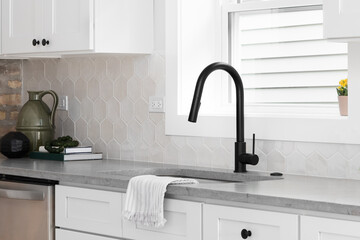 A beautiful kitchen sink detail with white cabinets, marble countertops, and a hexagon tiled...
