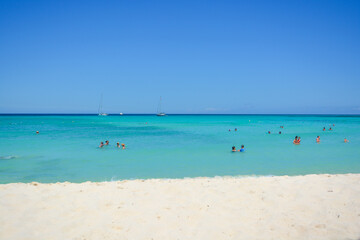 Fototapeta na wymiar Aruba, Caribbean island. A view on the blue sea, white sand and tourists swimming in azure water. 